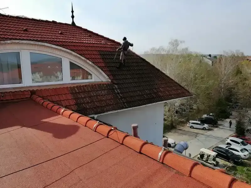 Szakember magasnyomású tetőtisztítást végez a cseréptetőn.